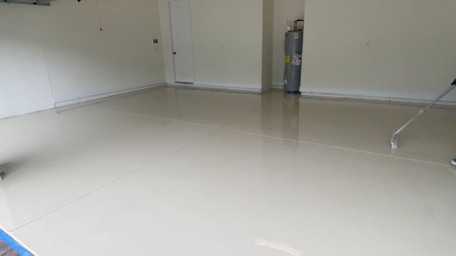 Empty residential garage with a cream solid-color coating still wet and glossy, a roller on a pole at the right edge, a water heater in the back corner