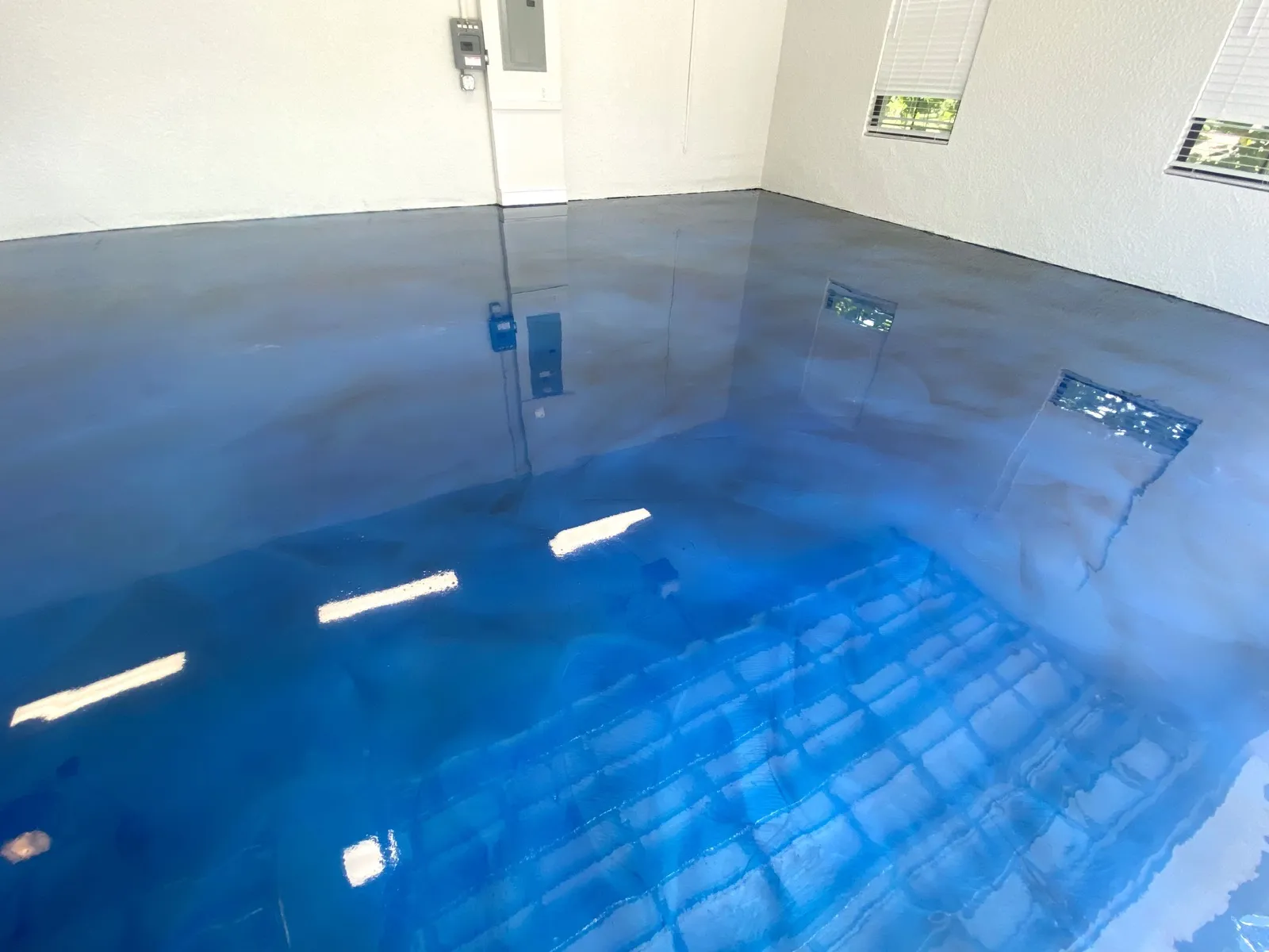 Blue metallic epoxy floor catching daylight through the window bay of a finished garage in Cape Coral, FL